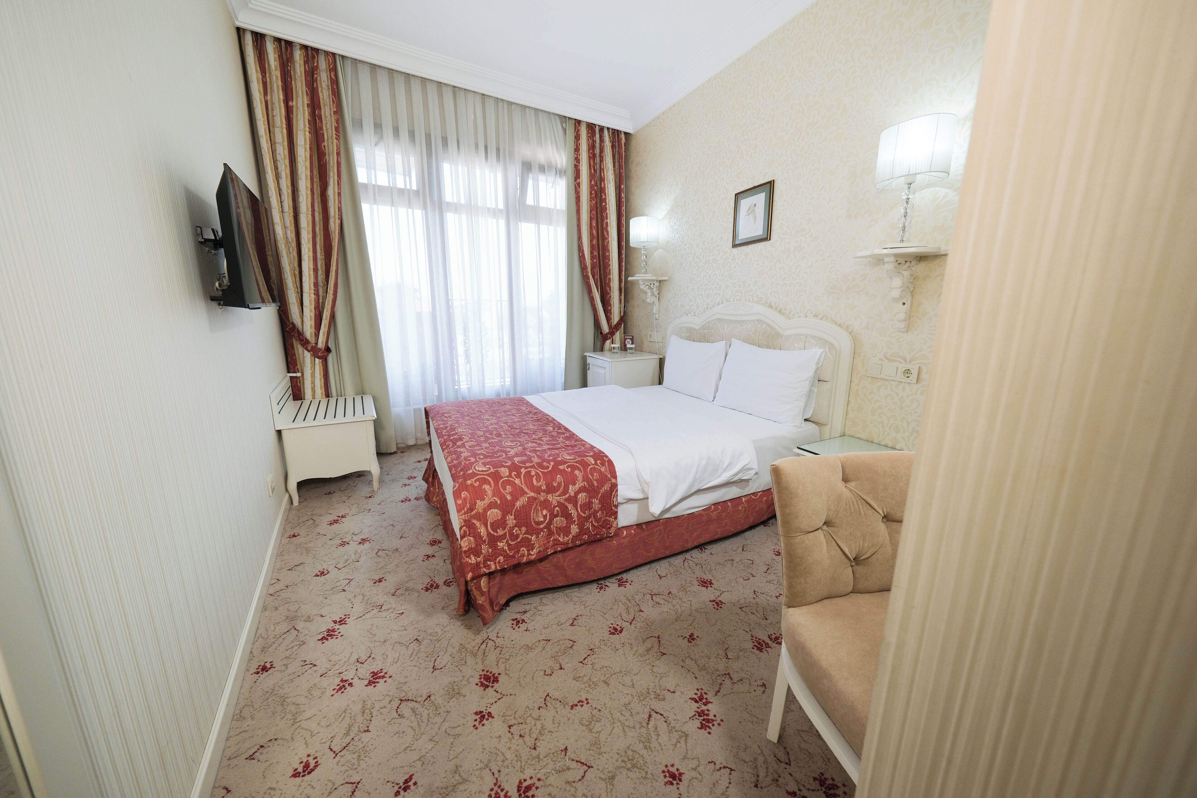 A hotel room with a bed, a bedside table, a lamp, a TV, and a chair.