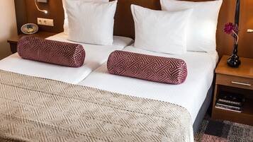 Een hotelkamer met een opgemaakt bed, een bedlampje, een nachtkastje met een bloevas en een klein dressoir.