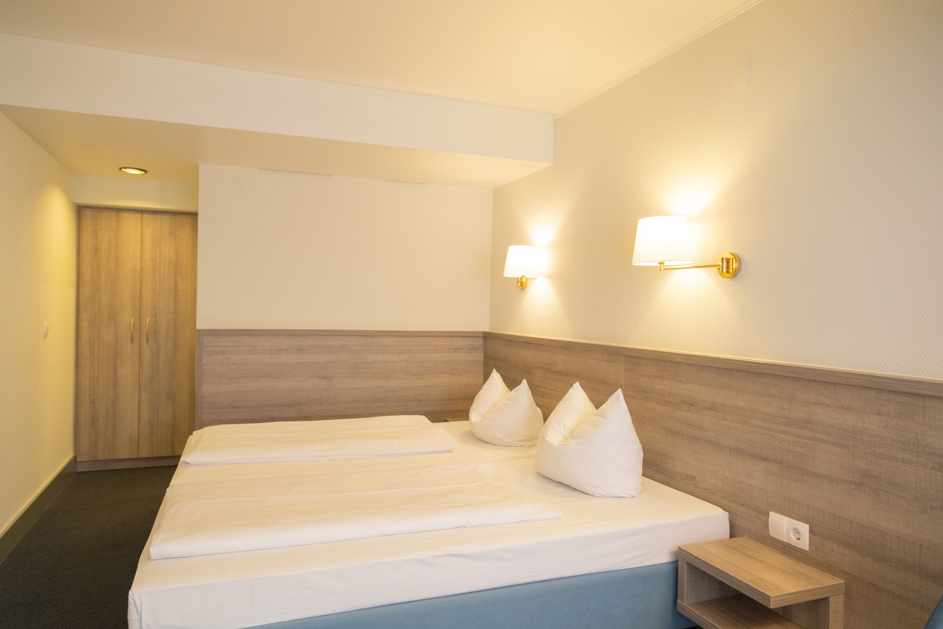A hotel room with a large bed, two bedside tables, a nightstand, and two wall-mounted lamps.