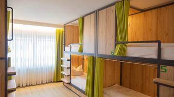 Een slaapkamer met stapelbedden, houten wanden en groene gordijnen, met een raam met dunne gordijnen en een houten vloer.