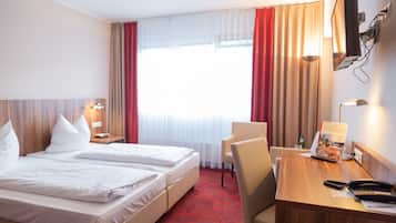 Une chambre d’hôtel équipée d’un lit, d’un bureau, d’une chaise, d’une télévision et d’une fenêtre avec des rideaux.