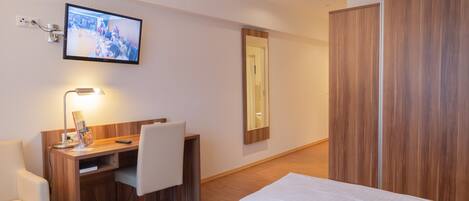 A hotel room with a bed, a desk with a chair, a TV mounted on the wall, and a wardrobe.