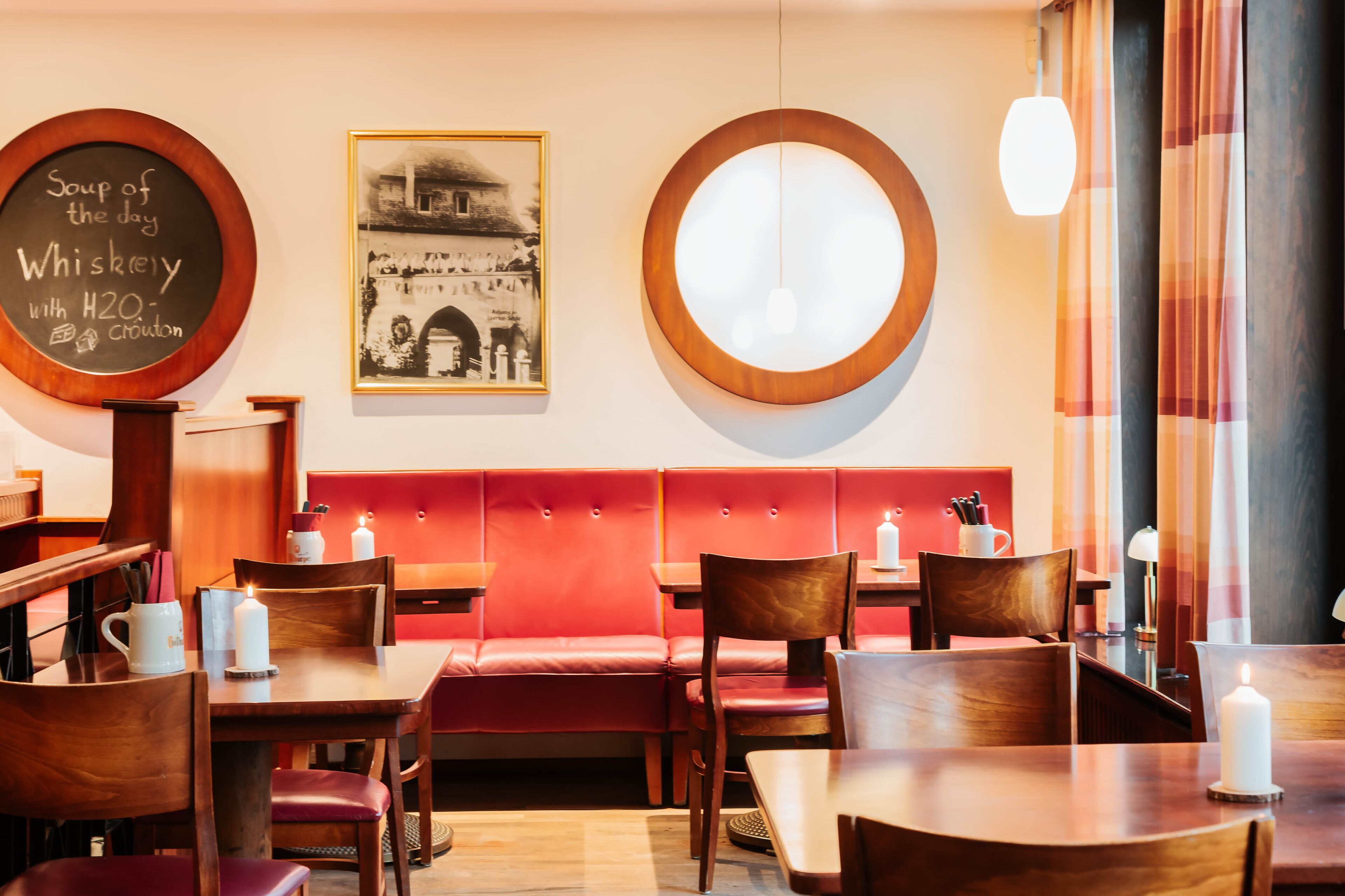 A restaurant interior with wooden tables and red cushioned booths, a chalkboard menu, and a framed historical photo on the wall.