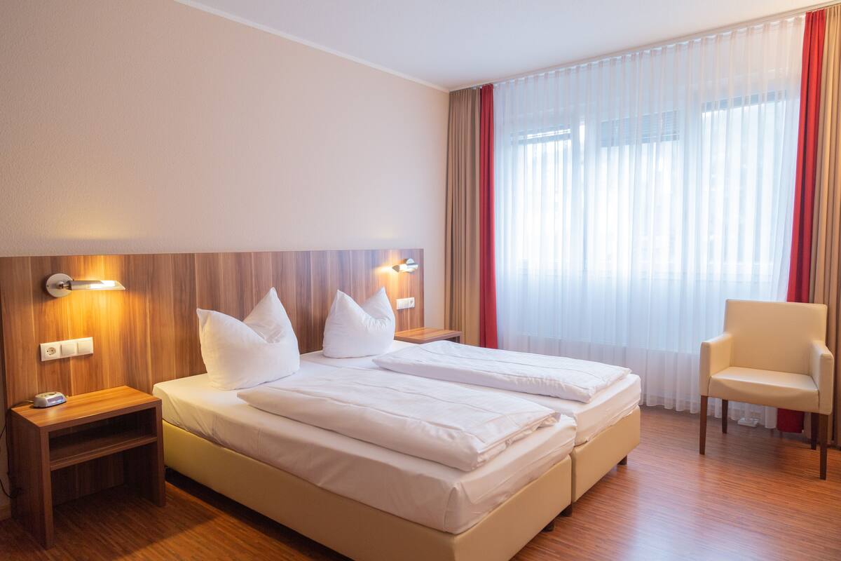 Une chambre d’hôtel avec un lit double, des tables de chevet, une chaise et une grande fenêtre avec des rideaux.