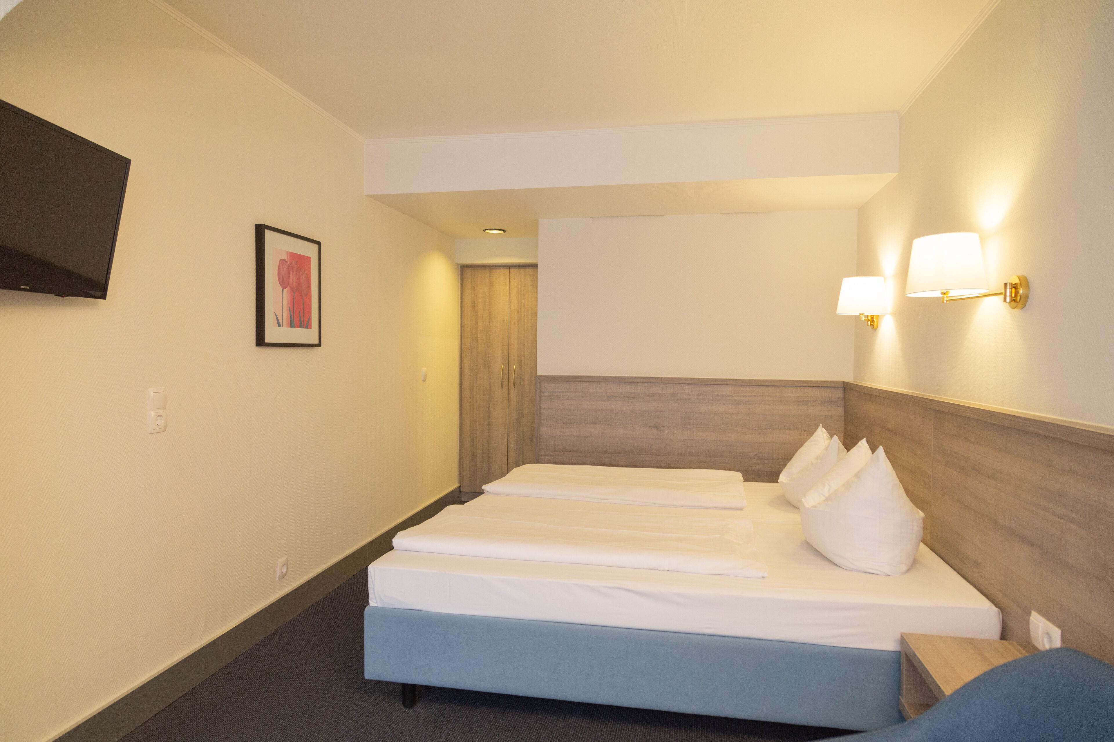 Habitación de hotel con dos camas, un televisor de pantalla plana, un cuadro enmarcado y lámparas fijadas a la pared.