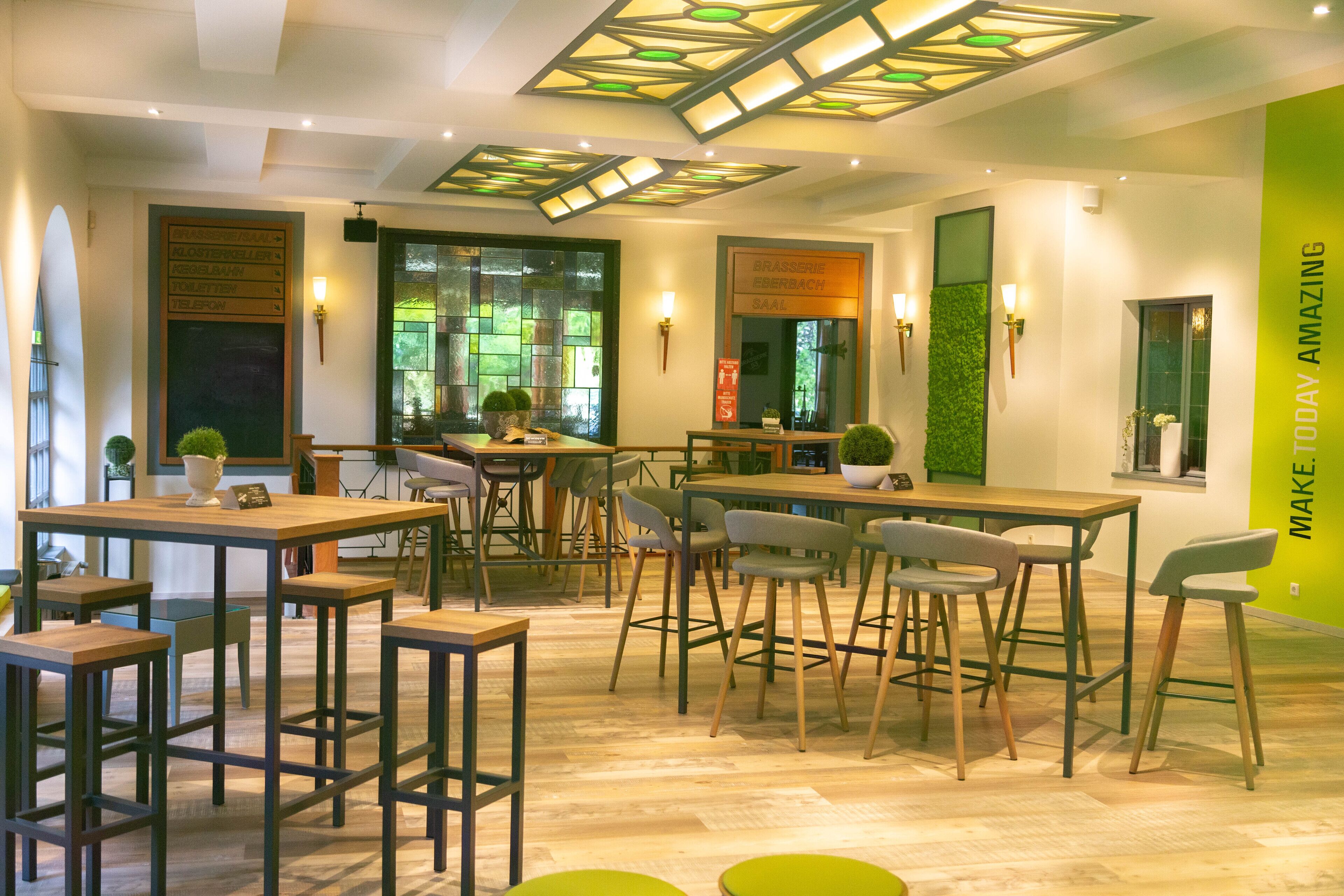 Un espace repas moderne avec plusieurs tables et chaises, un mur d’accent vert et un panneau sur lequel on peut lire : « FAITES EN SORTE QUE CETTE JOURNÉE SOIT INOUBLIABLE ».