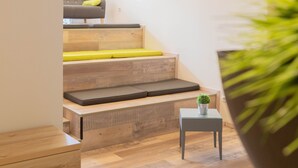 A modern interior with a staircase leading to a seating area, a small table with a plant, and a wall-mounted light fixture. - Das Ebertor Hotel & Hostel (Boppard)