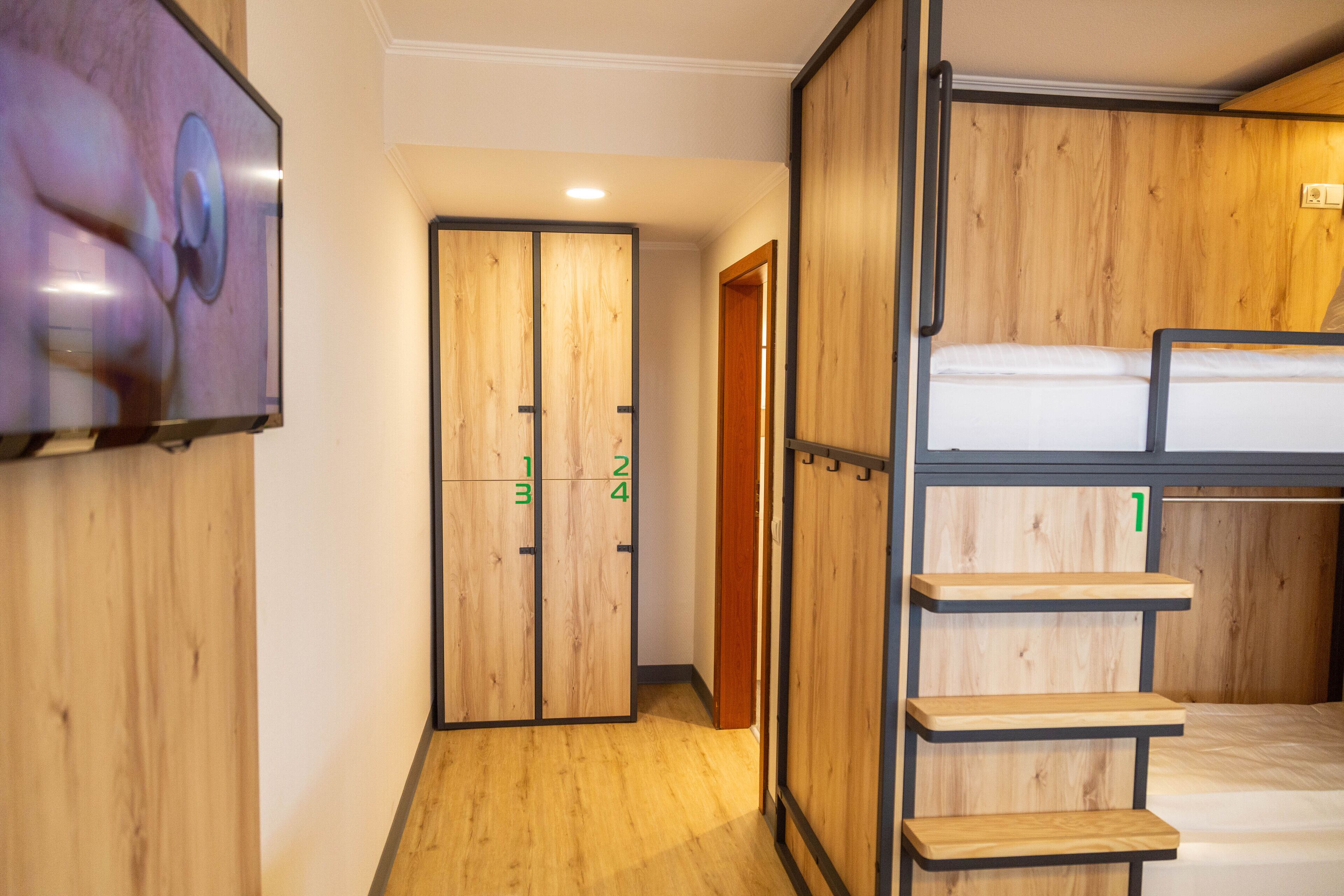 A room with a bunk bed, wooden walls, a TV mounted on the wall, and a door with numbered sections.