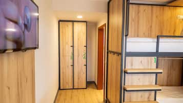 Habitación con literas, paredes de madera, un televisor montado en la pared y una puerta con divisiones numeradas.