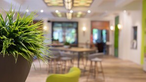 A modern interior with a large potted plant in the foreground, a dining area with chairs and tables, and a bright green accent wall. - Das Ebertor Hotel & Hostel (Boppard)