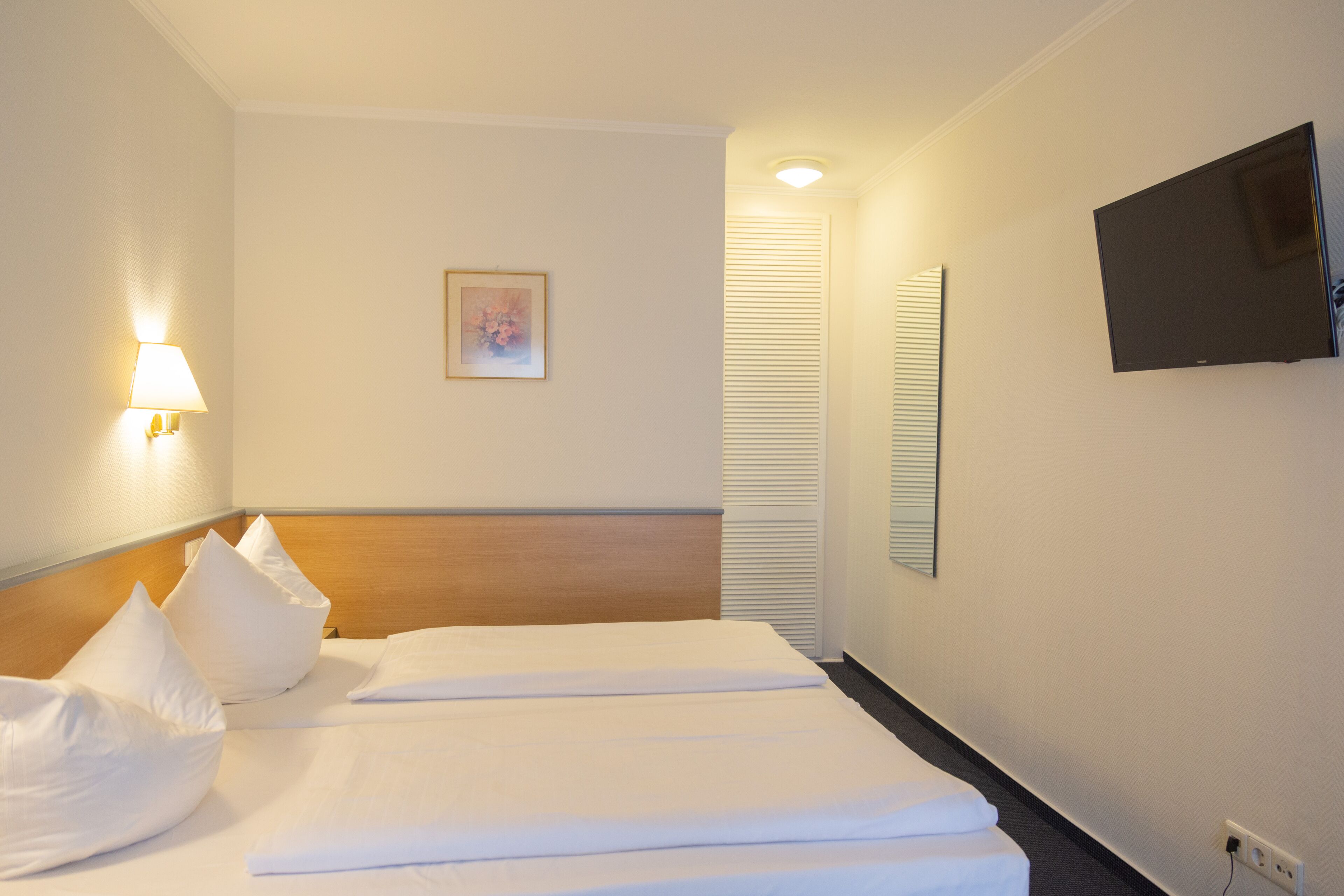 Een hotelkamer met twee bedden, een tv aan de muur en een bedlampje.