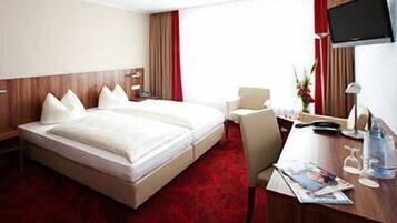 A hotel room with a large bed, a desk, a chair, a TV, and a red carpet.