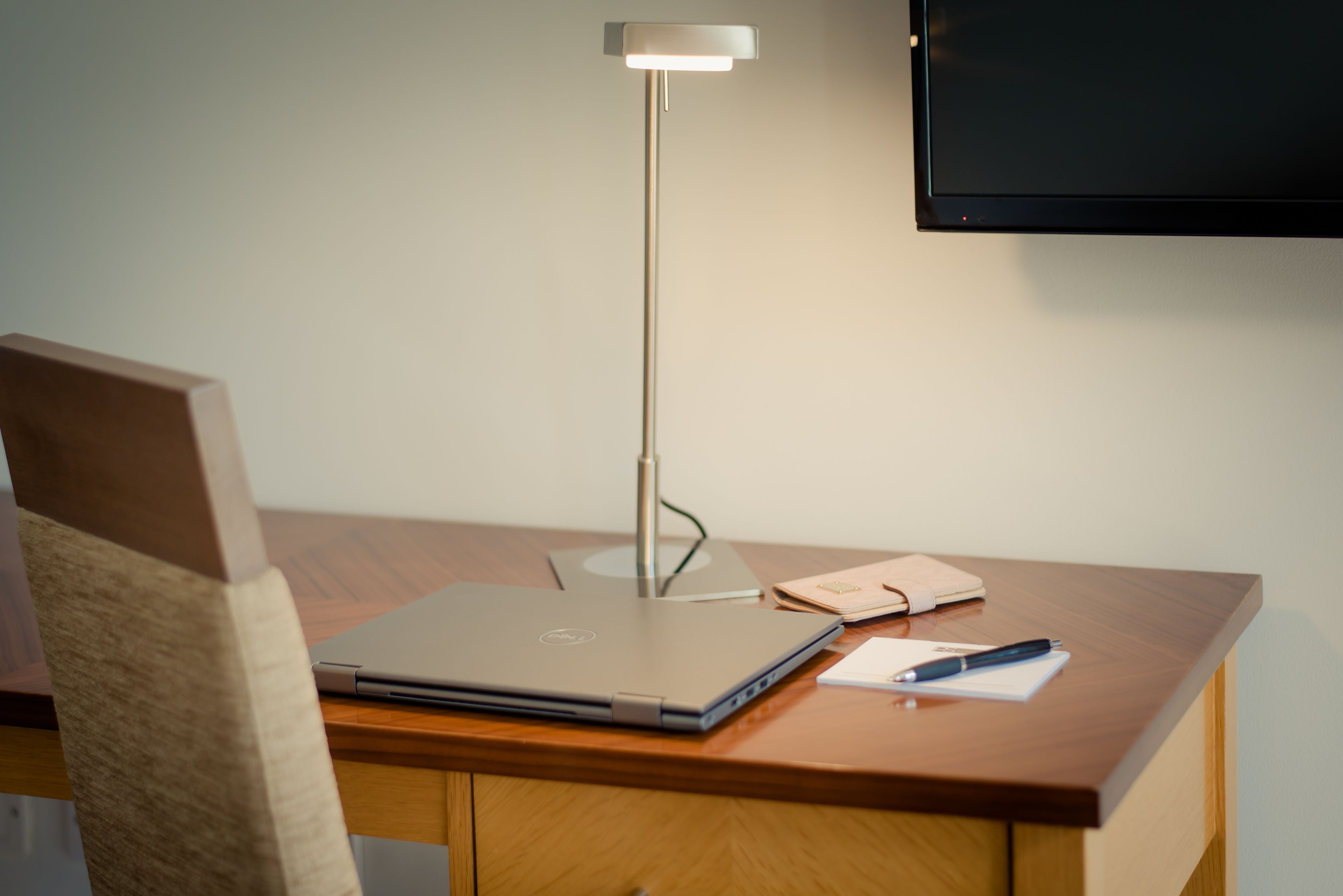 Un bureau en bois avec un ordinateur portable, une lampe, un carnet et un stylo.