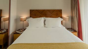 A hotel room with a large bed, two bedside tables, a wooden headboard, and a window with curtains.