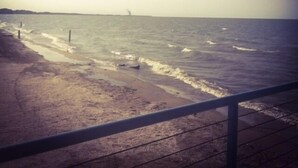 A beach with waves, a distant lighthouse, and a clear sky. - Beachfront Resort (Port Clinton)