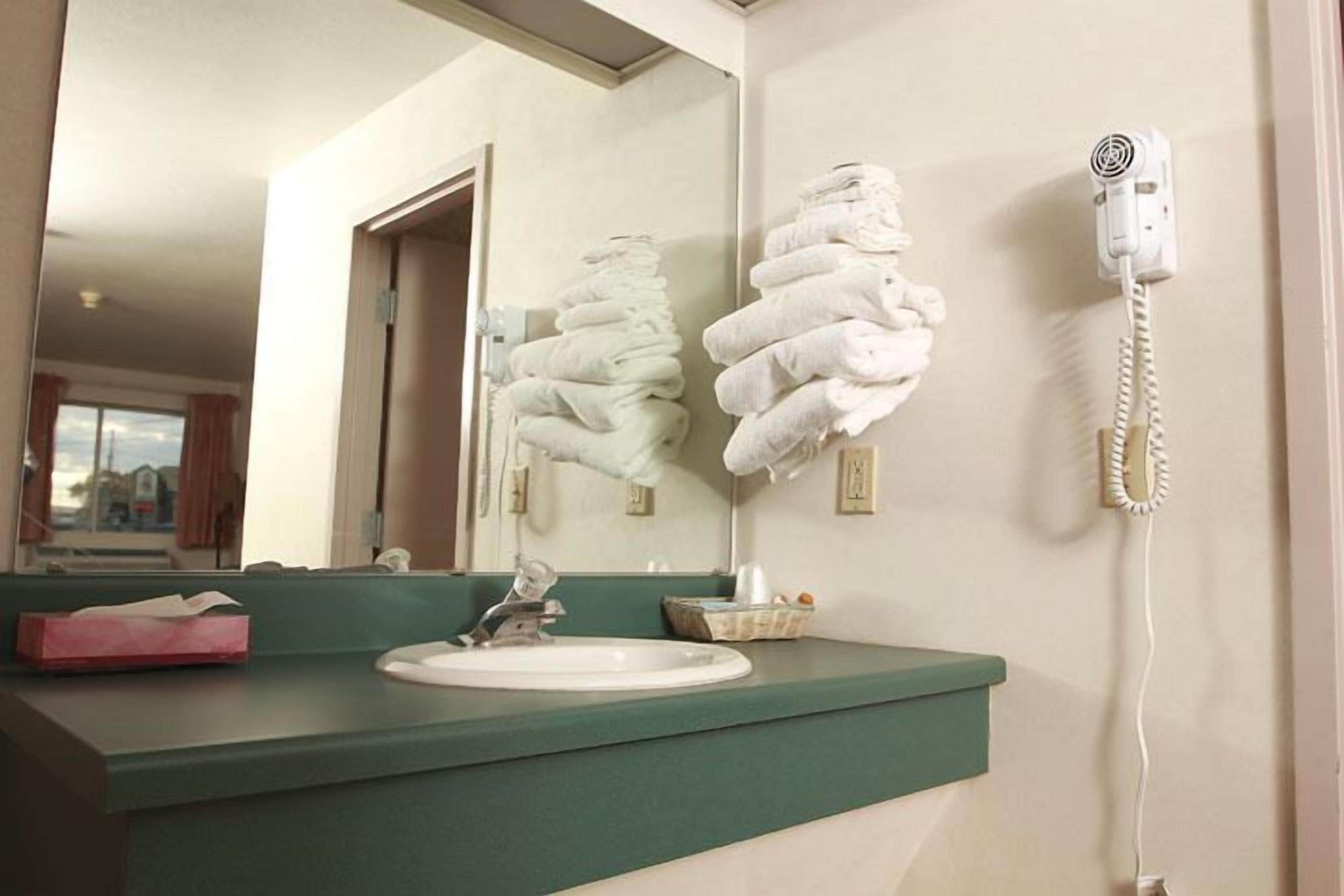 Un baño con lavamanos, espejo y secador de pelo sujeto a la pared.