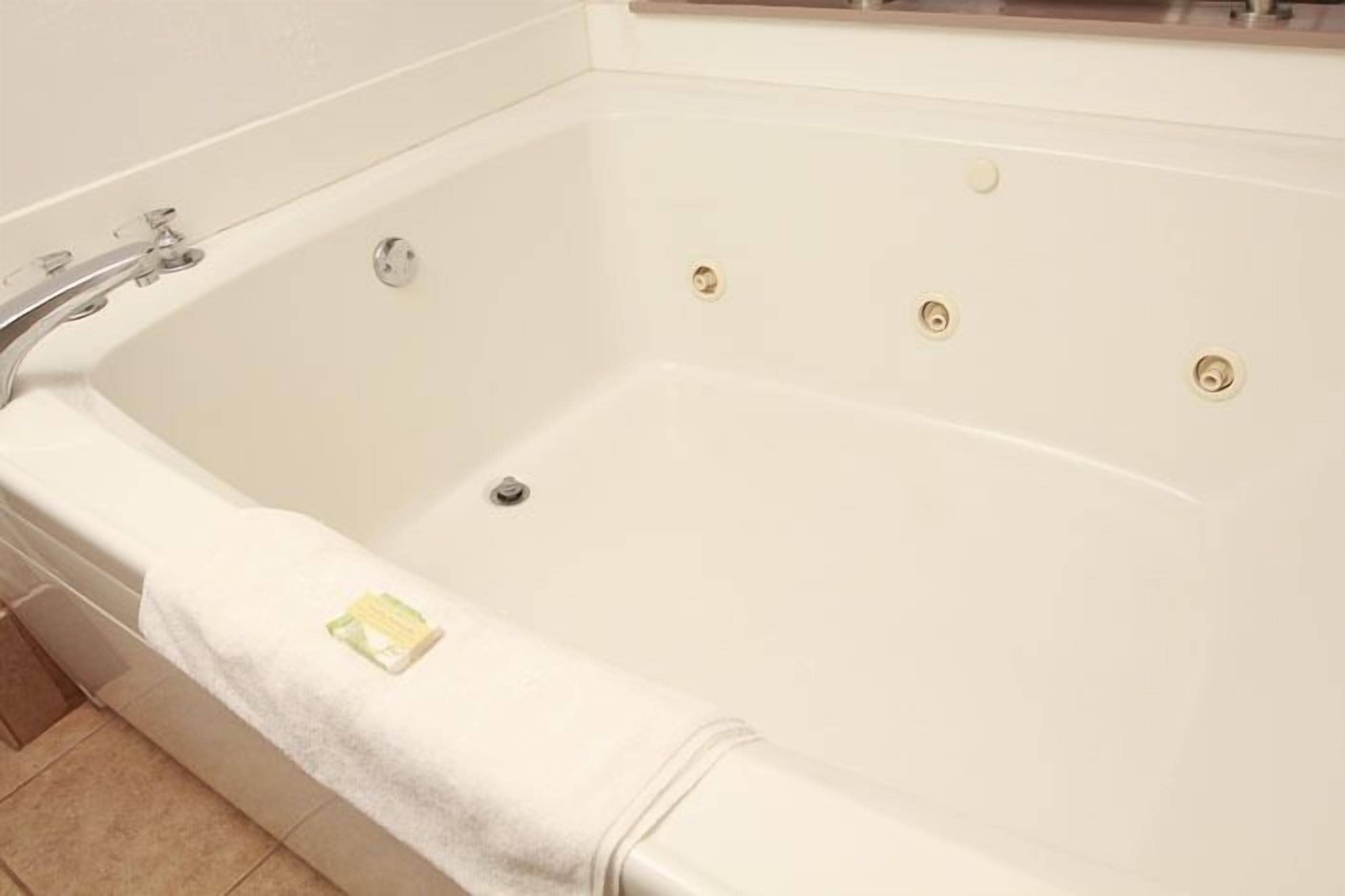 Una bañera blanca con un solo grifo y desagüe, una toalla al lado, y una pequeña botella de jabón.