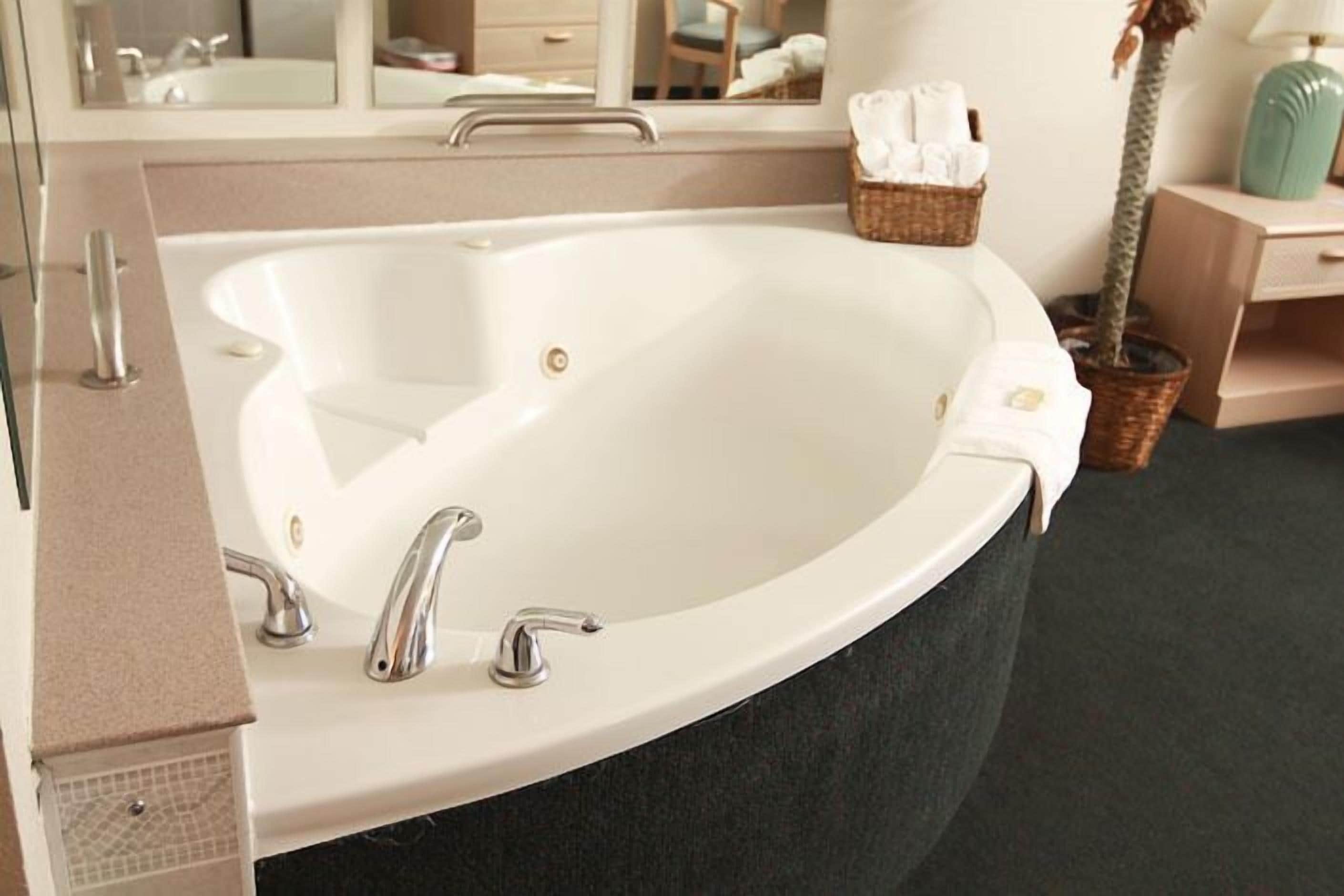 A large, curved bathtub with a single faucet and a small control knob, surrounded by a beige countertop and a dark floor.