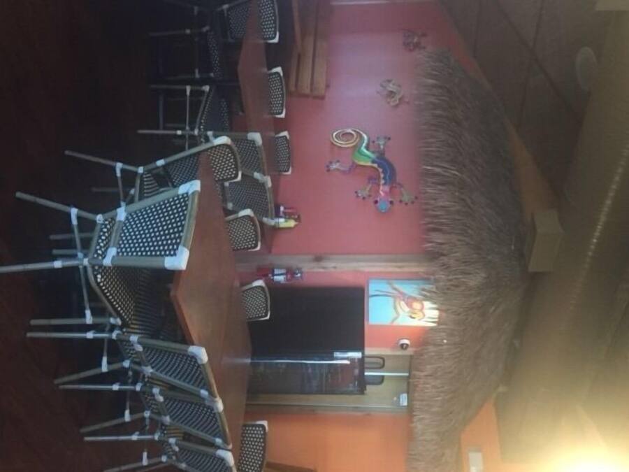 A restaurant with multiple tables and chairs, a thatched roof, and a mural on the wall.