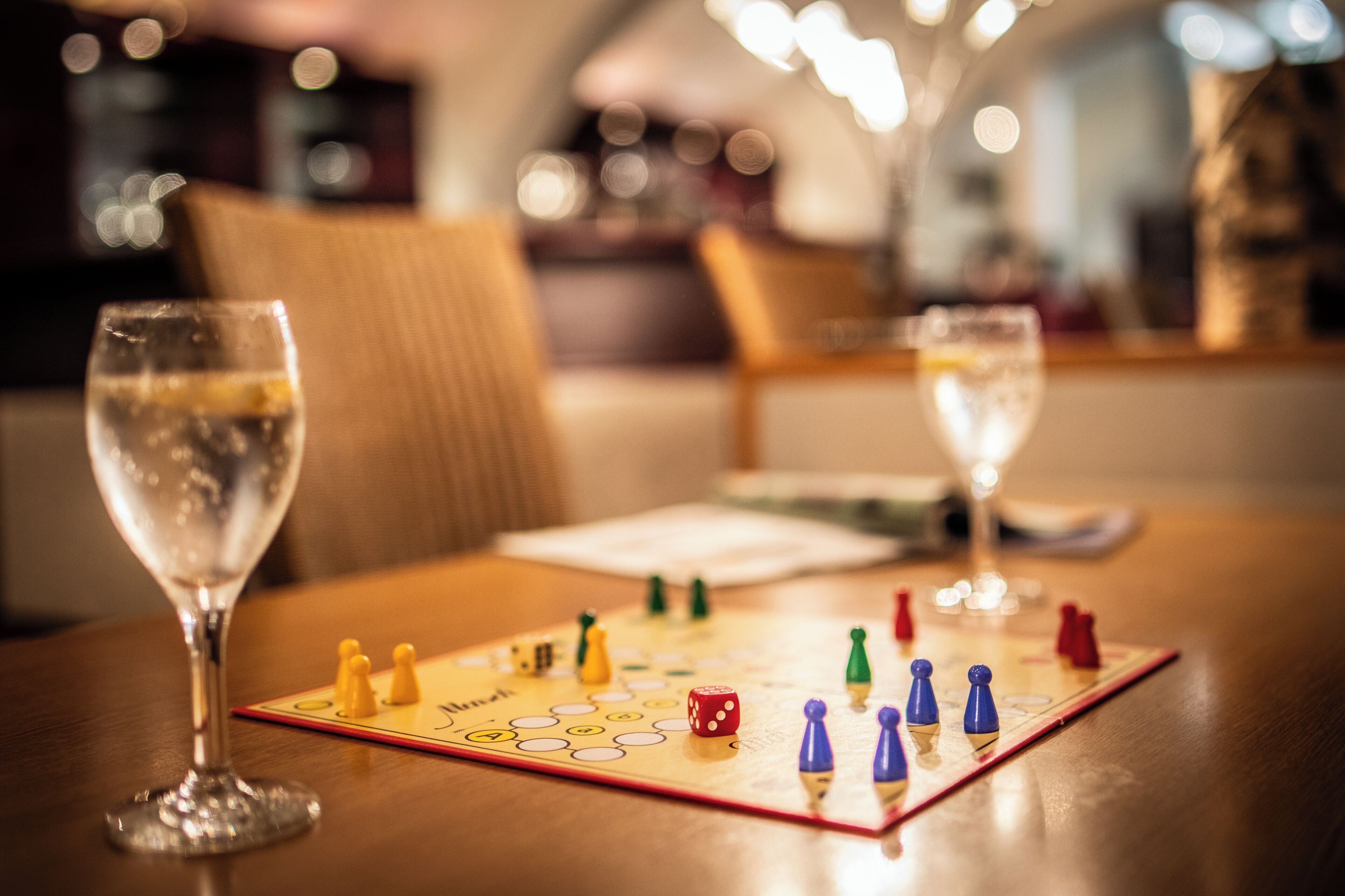 Un jeu de société est posé sur une table, à côté de verres contenant un liquide transparent.