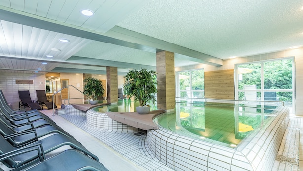Un espace piscine intérieur moderne, doté de sièges, d’un élément décoratif aquatique et de grandes fenêtres.