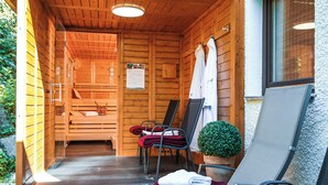Une cabane en bois dotée d’une véranda, d’un espace douche et d’un coin salon avec des chaises et une table.