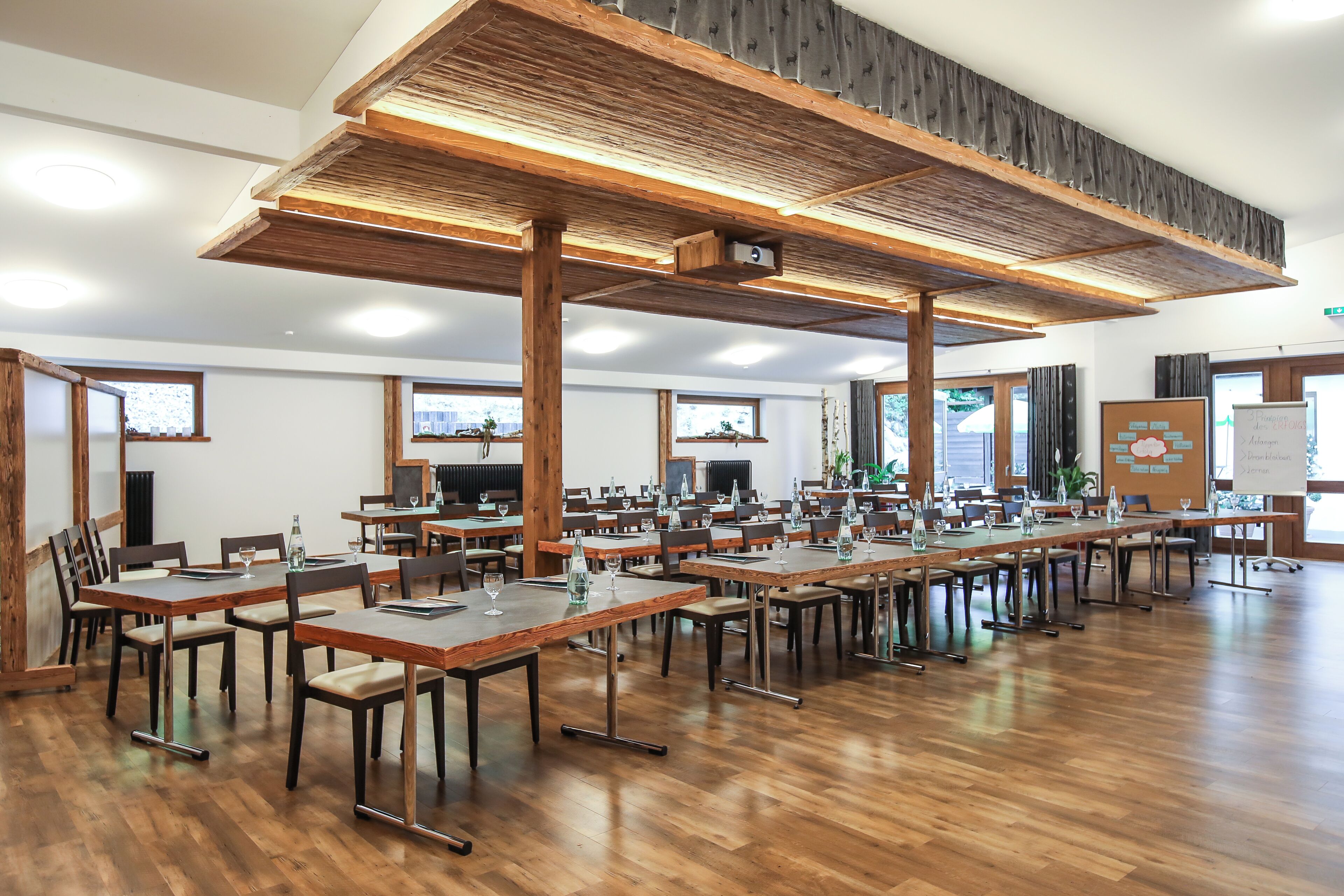 Ein geräumiger Konferenzraum mit langen Tischen, Holzbalken und großen Fenstern.