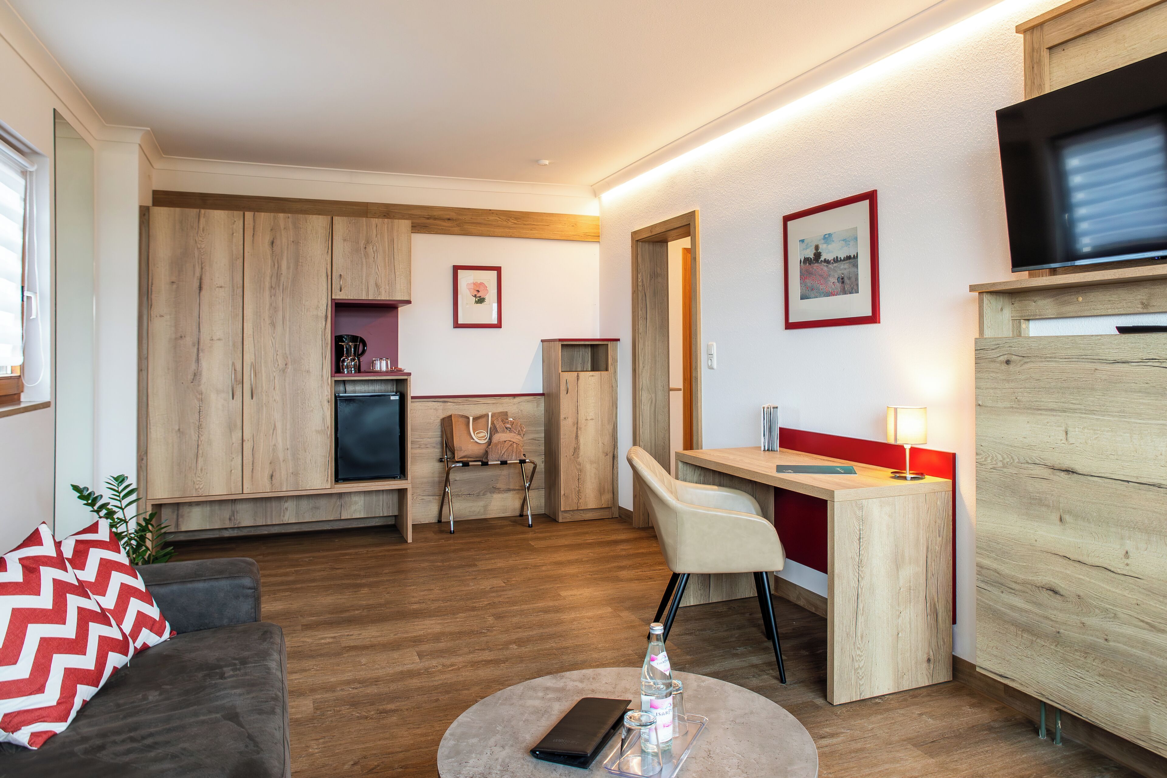 Una sala de estar moderna con sofá, un comedor con mesa y sillas, una kitchenette y un televisor montado en la pared.