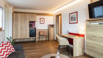 Una sala de estar moderna con sofá, un comedor con mesa y sillas, una kitchenette y un televisor montado en la pared.