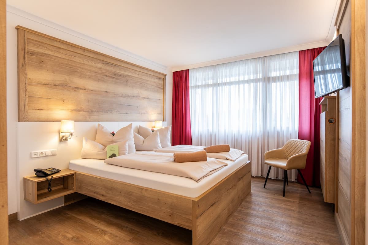 A hotel room with a wooden bed, bedside lamps, a chair, and a TV.