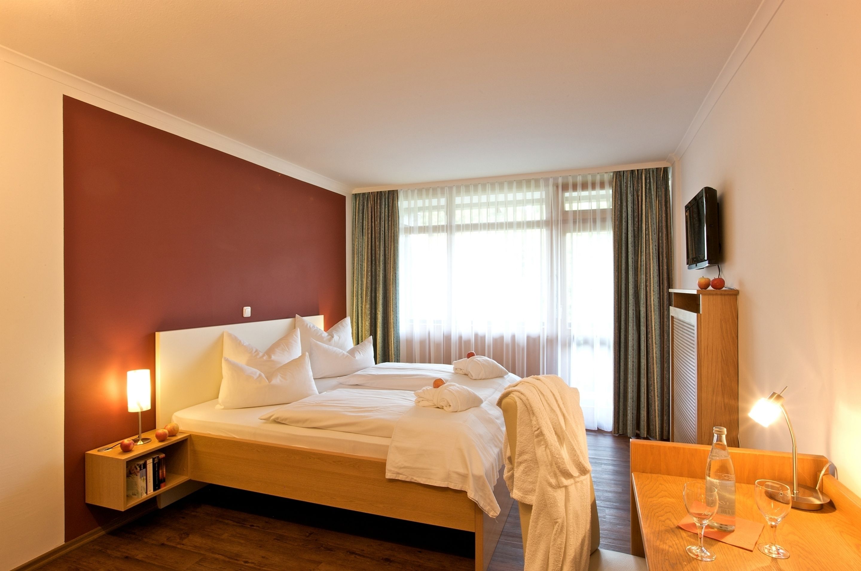 Ein Hotelzimmer mit Bett, Nachttisch, Fernseher und einem Fenster mit Vorhängen.