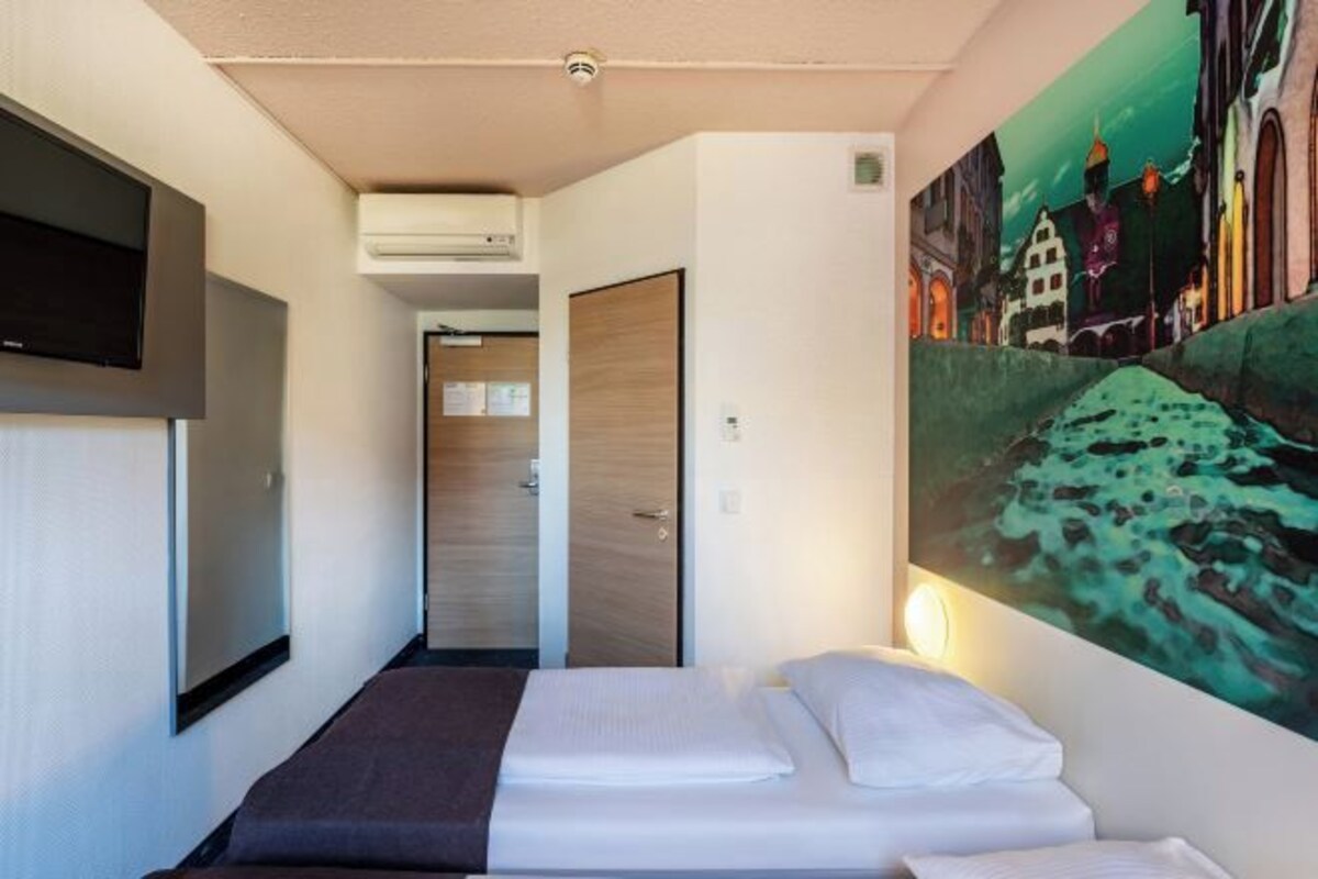 Una habitación de hotel con una cama, un cuadro en la pared y un televisor montado.