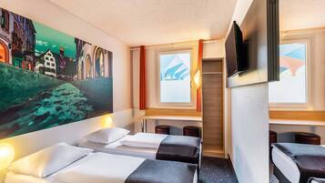 Een hotelkamer met twee bedden, een stadslandschap schilderij, een televisie en een raam met gordijnen.