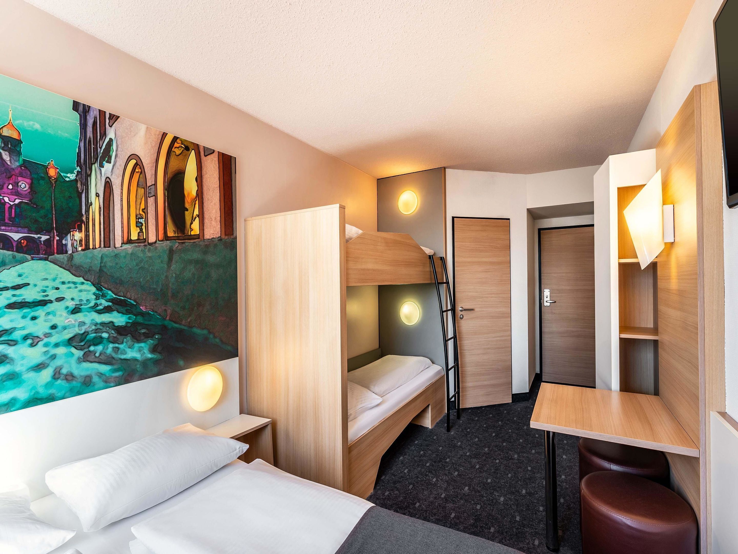 Une chambre d’hôtel compacte avec des lits superposés, un bureau et un petit coin salon.
