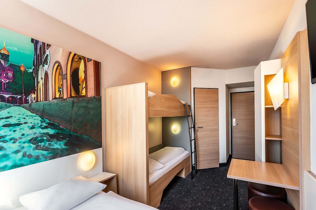 Une chambre d’hôtel compacte avec des lits superposés, un bureau et un petit coin salon.