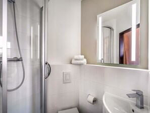 Une salle de bain moderne avec une douche à l’italienne en verre, un lavabo blanc et un miroir au-dessus du lavabo.