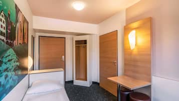 A hotel room with a bed, a desk, a wall-mounted light, and a door.