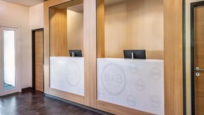A reception area with a modern design, featuring a wooden reception desk and a glass partition. - B&B Hotel Freiburg-Nord (Freiburg im Breisgau)