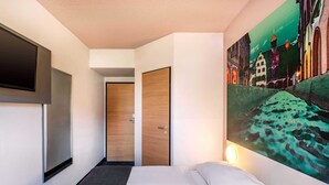 A hotel room with a bed, a painting on the wall, and a TV mounted on the wall. - B&B Hotel Freiburg-Nord (Freiburg im Breisgau)
