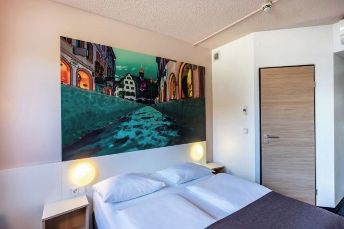 Una habitación de hotel con una cama, dos mesitas de noche, una lámpara de pared y una puerta.
