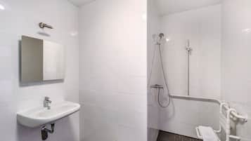 A bathroom with white tiles, a sink, a mirror, and a shower area with a grab bar.