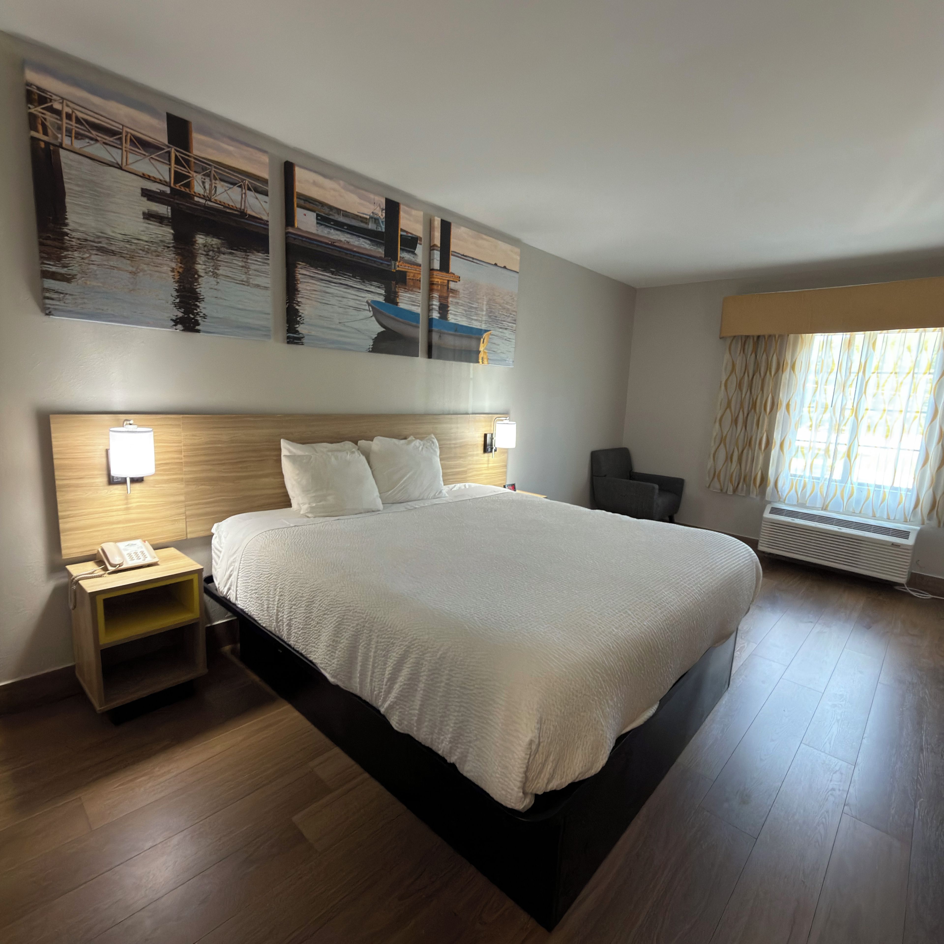 A hotel room with a large bed, a nightstand with a phone, a wall-mounted lamp, and a window with curtains.