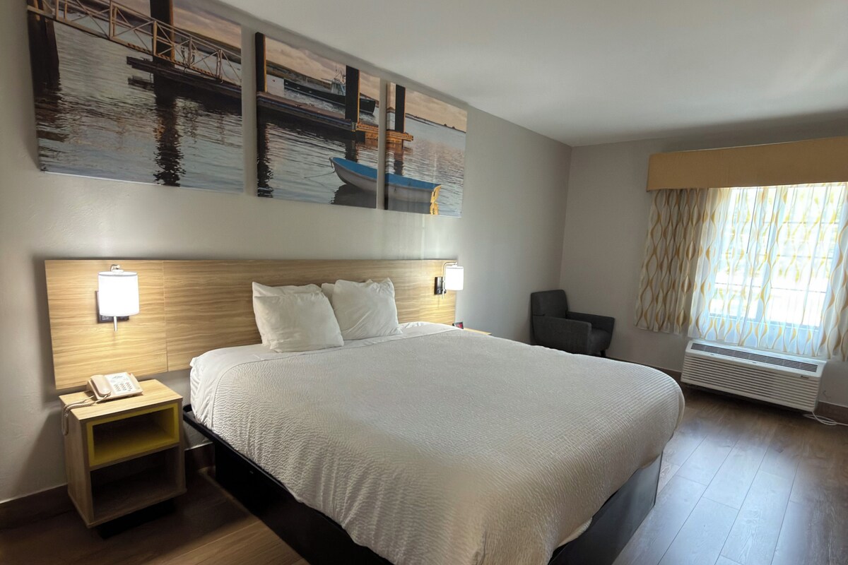 A hotel room with a large bed, a nightstand with a phone, a wall-mounted lamp, and a window with curtains.
