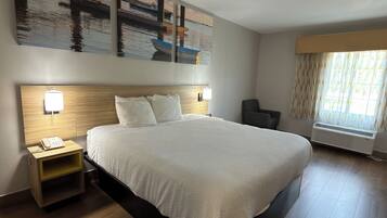 A hotel room with a large bed, a nightstand with a phone, a wall-mounted lamp, and a window with curtains.
