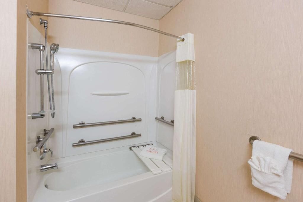 A bathroom with a bathtub, shower, and handrails.