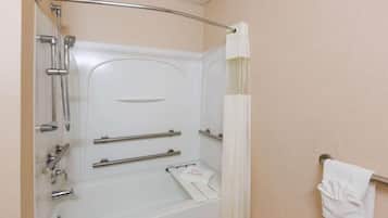 A bathroom with a bathtub, shower, and handrails.