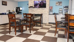 Un restaurant avec un sol à carreaux, des tables et des chaises en bois, un mur décoratif en pierre, un téléviseur à écran plat et des appareils de cuisine.
