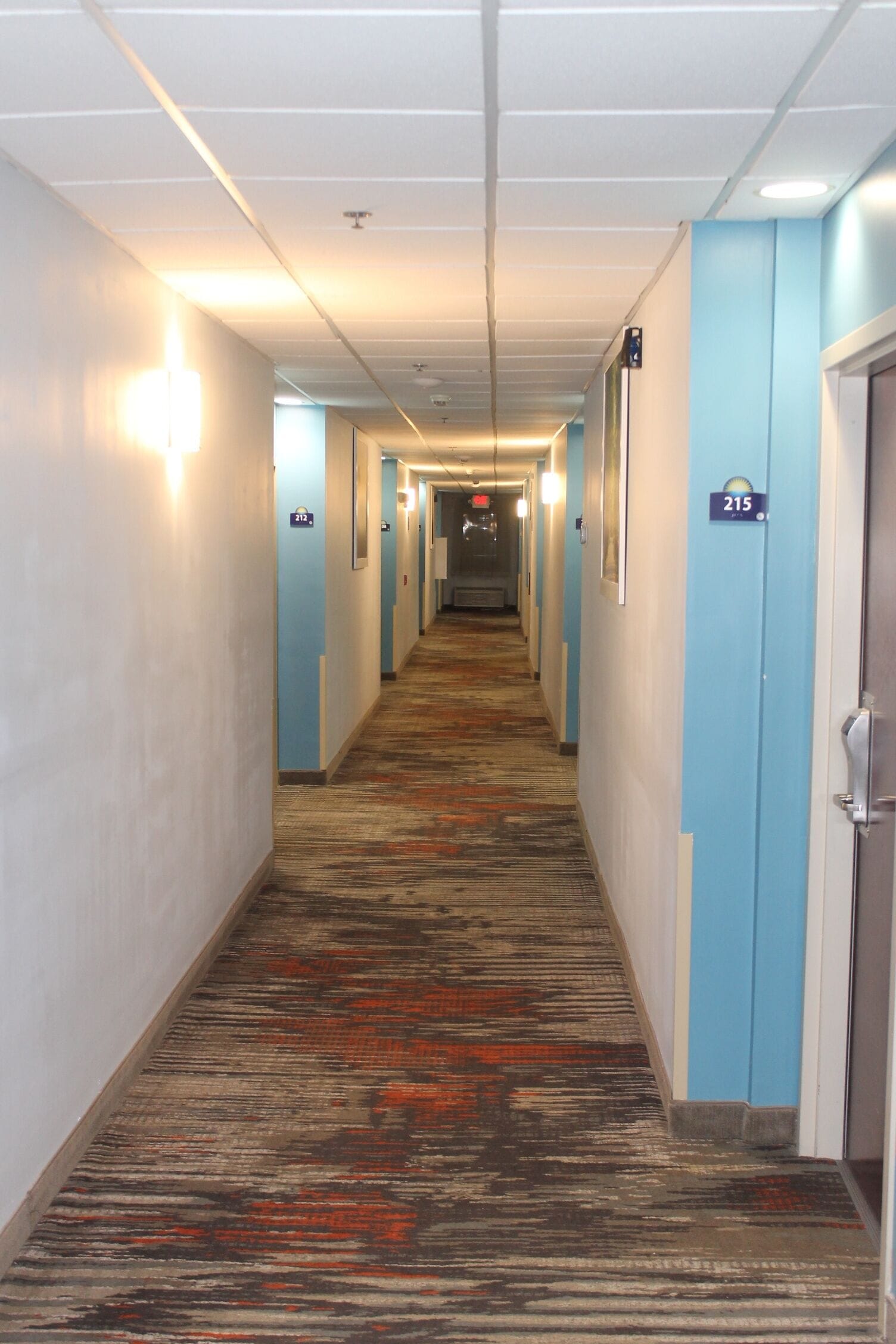 Un passadís d'hotel amb sòls de catifes, parets blaves clares i portes numerades.