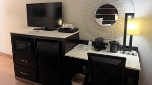 Une chambre d’hôtel équipée d’un bureau, d’une télévision, d’un four à micro-ondes, d’une machine à café, d’une poubelle et d’une chaise.