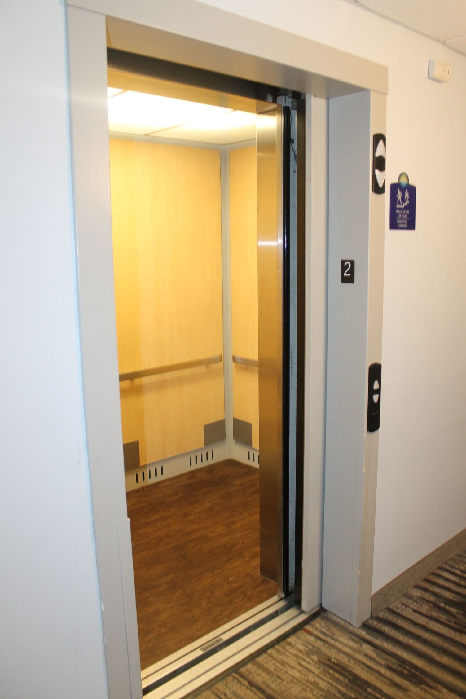 Un ascenseur avec un intérieur en bois, une porte portant une plaque avec un numéro, et un panneau indiquant un espace réservé aux fumeurs.